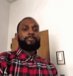 A Man With A Beard Wearing A Red And Black Plaid Shirt Is Standing In A Room . GIF