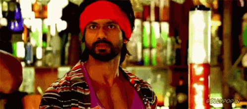 A Man With A Beard Wearing A Red Headband And A Striped Shirt Is Standing In Front Of A Bar . GIF