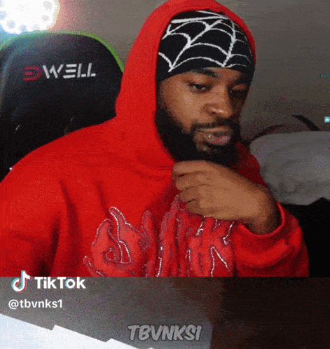 A Man With A Beard Wearing A Red Hoodie And A Black And White Spider Web Hat GIF