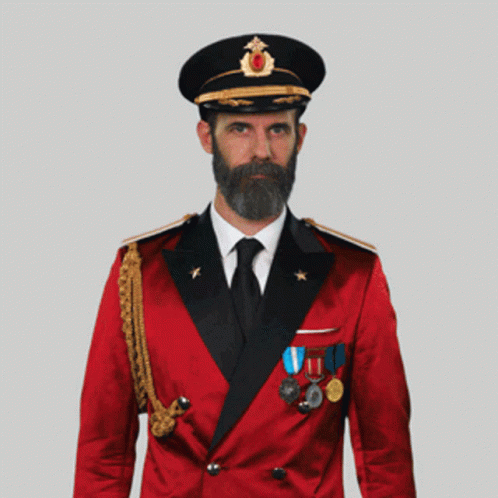 A Man With A Beard Wearing A Red Suit And Black Hat Salutes GIF