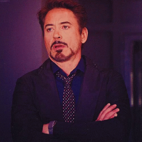 A Man With A Beard Wearing A Suit And Tie Has His Arms Crossed GIF