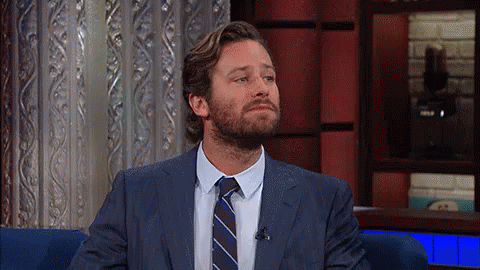 A Man With A Beard Wearing A Suit And Tie Is Sitting In A Chair . GIF