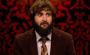 A Man With A Beard Wearing A Suit And Tie Is Standing In Front Of A Red Wall . GIF