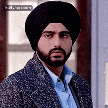 A Man With A Beard Wearing A Turban And A Jacket Is Looking At The Camera . GIF