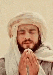 A Man With A Beard Wearing A Turban Is Praying With His Eyes Closed . GIF