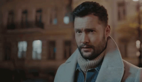 A Man With A Beard Wearing A White Coat And A Turtleneck Sweater . GIF