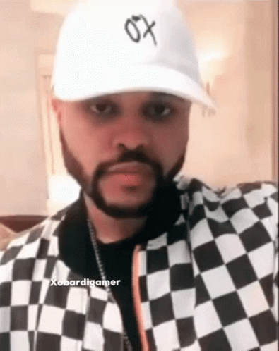 A Man With A Beard Wearing A White Hat And A Black And White Checkered Jacket . GIF