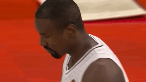 A Man With A Beard Wearing A White Jersey Looks Down At Something GIF