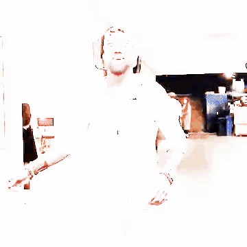 A Man With A Beard Wearing A White Shirt And A Baseball Cap Is Walking Down A Hallway . GIF