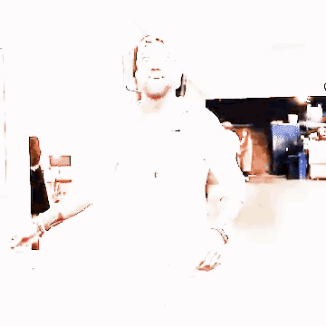 a man with a beard wearing a white shirt and a baseball cap is walking down a hallway .