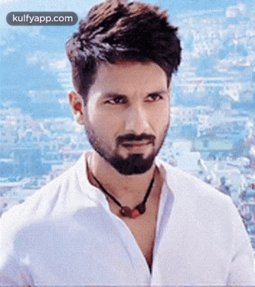 A Man With A Beard Wearing A White Shirt And A Necklace Is Looking At The Camera . GIF