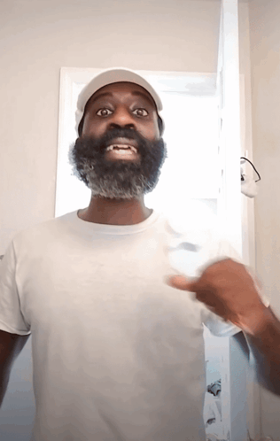 A Man With A Beard Wearing A White Shirt And Hat GIF