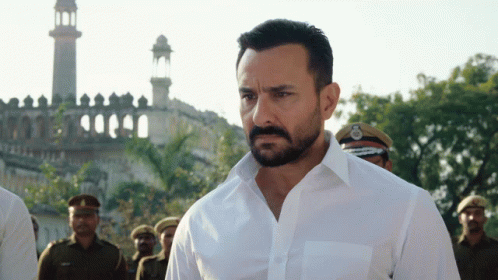 A Man With A Beard Wearing A White Shirt Is Standing In Front Of A Mosque GIF