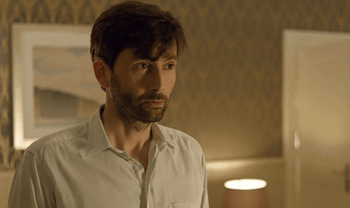 A Man With A Beard Wearing A White Shirt Looks At The Camera GIF