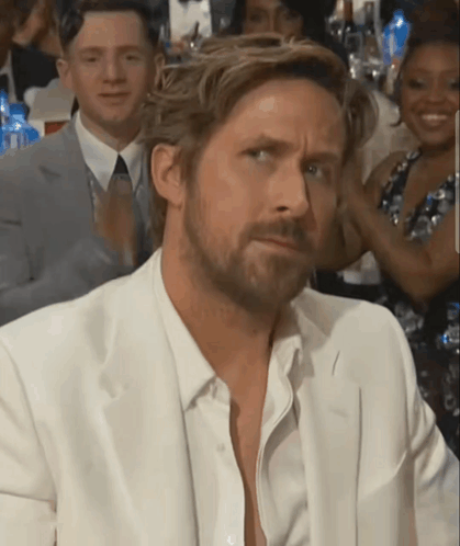 A Man With A Beard Wearing A White Suit Looks At The Camera GIF