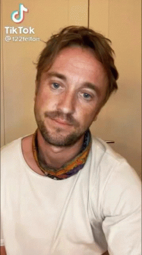 A Man With A Beard Wearing A White T-Shirt And A Scarf Around His Neck GIF