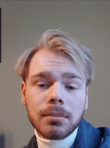 A Man With A Beard Wearing A White Turtleneck Looks At The Camera GIF