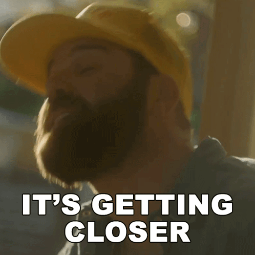 A Man With A Beard Wearing A Yellow Hard Hat Says It 'S Getting Closer GIF