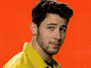 A Man With A Beard Wearing A Yellow Jacket And A Black Shirt Is Smiling . GIF