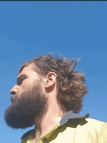A Man With A Beard Wearing A Yellow Shirt Looks To The Side GIF