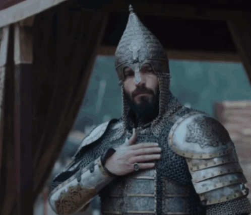 a man with a beard wearing armor and a helmet with his hand on his chest