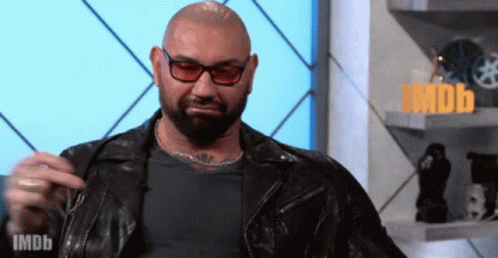 A Man With A Beard Wearing Glasses And A Leather Jacket Says Imdb On The Bottom Right GIF