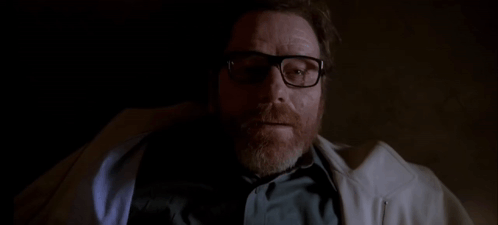 A Man With A Beard Wearing Glasses And A White Coat Is Laying Down In A Dark Room . GIF