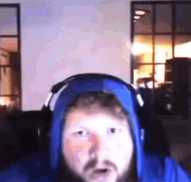 A Man With A Beard Wearing Headphones And A Blue Hoodie Is Sitting In Front Of A Computer Screen . GIF
