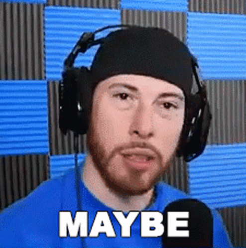 A Man With A Beard Wearing Headphones And A Blue Shirt Is Talking Into A Microphone . GIF