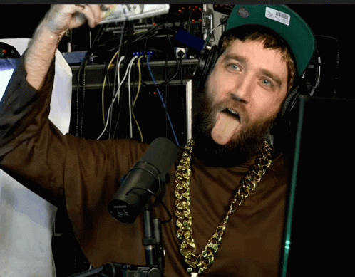 A Man With A Beard Wearing Headphones And A Shure Microphone Sticking Out His Tongue GIF
