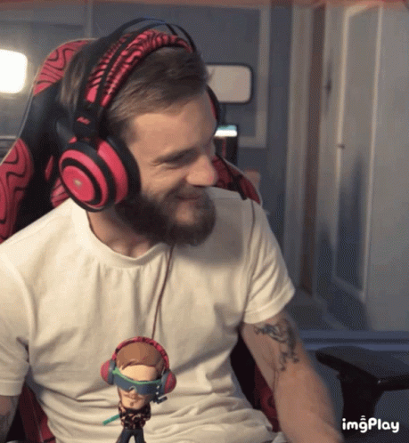 A Man With A Beard Wearing Headphones And Holding A Figurine That Says ' Imgplay ' On It GIF