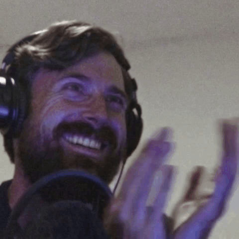 A Man With A Beard Wearing Headphones Is Smiling And Clapping GIF