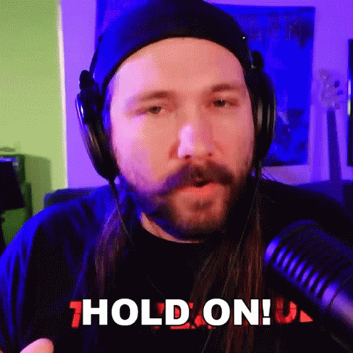 A Man With A Beard Wearing Headphones Says " Hold On " GIF