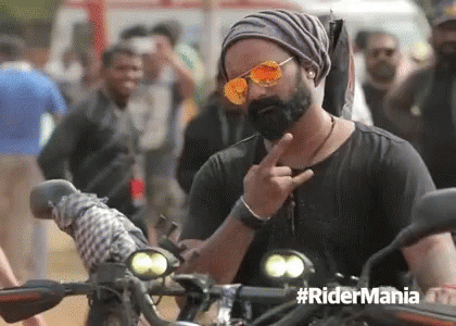 a man with a beard wearing sunglasses and a beanie is giving the middle finger while riding a motorcycle .