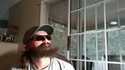 A Man With A Beard Wearing Sunglasses And A Hat Is Smoking A Cigarette GIF
