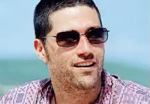 A Man With A Beard Wearing Sunglasses And A Pink Shirt Is Smiling . GIF