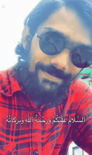 A Man With A Beard Wearing Sunglasses And A Plaid Shirt With Arabic Writing GIF