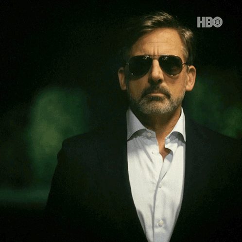 A Man With A Beard Wearing Sunglasses And A Suit With The Hbo Logo Behind Him GIF
