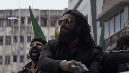 A Man With A Beard Wearing Sunglasses And Holding A Green Flag GIF