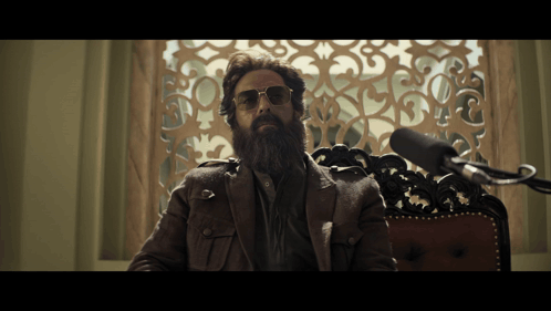 A Man With A Beard Wearing Sunglasses Sits In Front Of A Microphone GIF