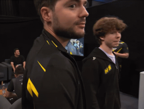 A Man With A Beard Wears A Black And Yellow Jacket That Says Nm GIF