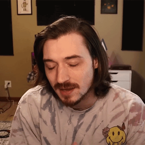a man with a beard wears a tie dye shirt with a smiley face on the front