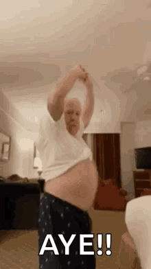 A Man With A Big Belly Is Dancing In A Living Room With His Shirt Off . GIF