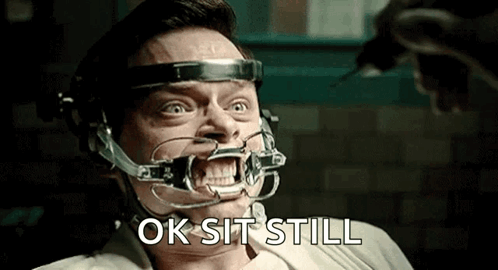 A Man With A Brace On His Teeth Is Sitting In A Chair And Says Ok Sit Still . GIF
