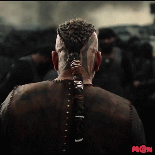 A Man With A Braided Ponytail And A Tattoo On His Face Is Standing In Front Of A Crowd GIF