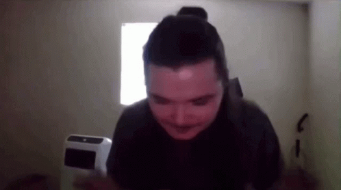 A Man With A Bun On His Head Is Standing In Front Of A Window In A Dark Room GIF