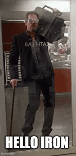 A Man With A Cane Is Carrying A Suitcase On His Shoulders And Says Hello Iron GIF
