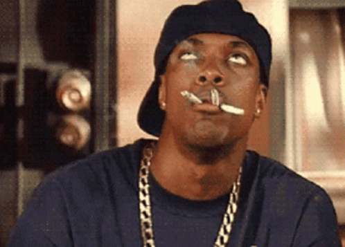 A Man With A Cigarette In His Mouth Wearing A Hat And Chains GIF