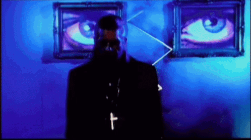 A Man With A Cross Around His Neck Is Standing In Front Of Two Large Eyes GIF