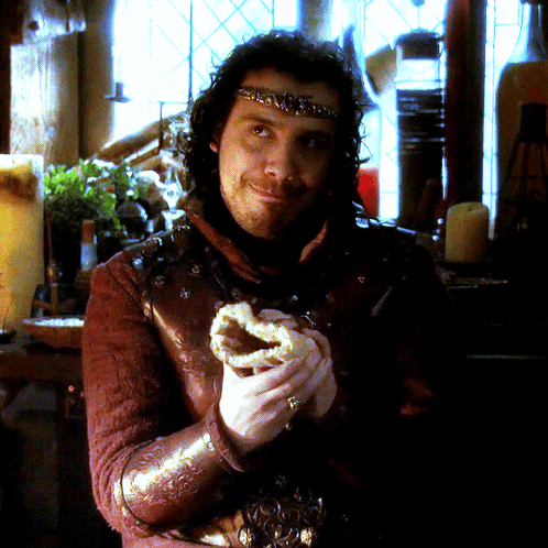 A Man With A Crown On His Head Is Holding A Pastry GIF